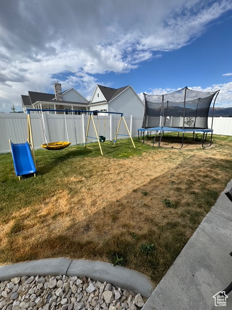 Fenced backyard featuring a trampoline and a playground