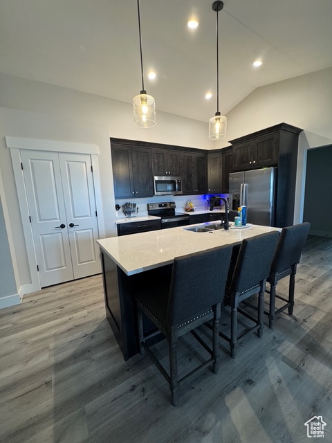 Kitchen featuring stainless steel appliances, light wood-style floors, lofted ceiling, a breakfast bar area, and an island with sink
