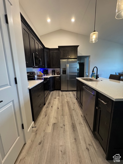 Kitchen featuring stainless steel appliances, vaulted ceiling, light wood-style floors, decorative light fixtures, and a kitchen island with sink