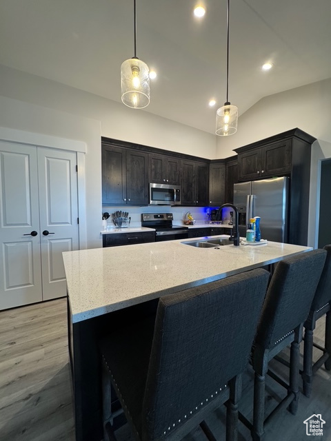 Kitchen with stainless steel appliances, light wood-style flooring, light stone counters, hanging light fixtures, and lofted ceiling