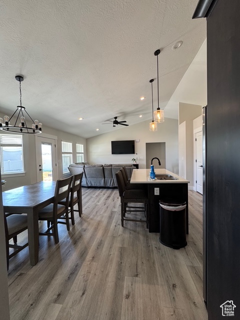Dining space with a textured ceiling, lofted ceiling, light wood-type flooring, a chandelier, and a ceiling fan