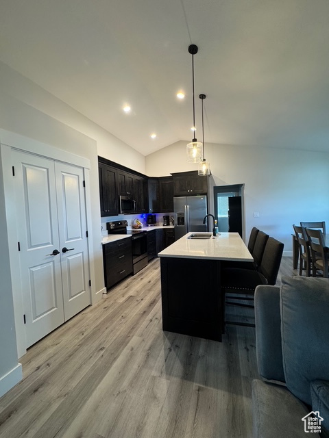 Kitchen featuring appliances with stainless steel finishes, open floor plan, light wood finished floors, light countertops, and vaulted ceiling