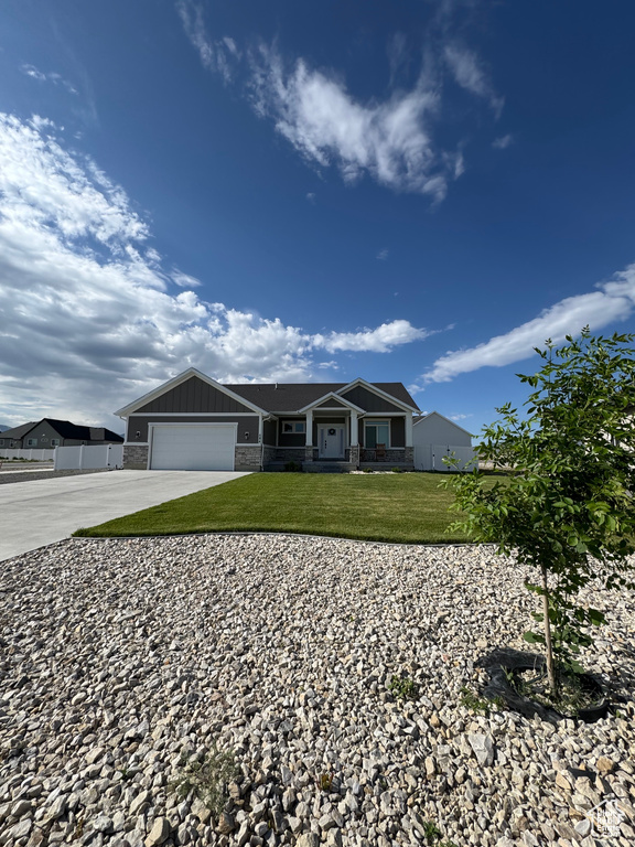 Ranch-style home featuring concrete driveway, a front lawn, a garage, and stone siding