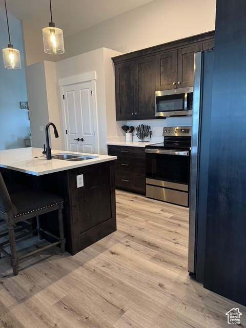 Kitchen with appliances with stainless steel finishes, light wood-type flooring, light countertops, pendant lighting, and a breakfast bar area