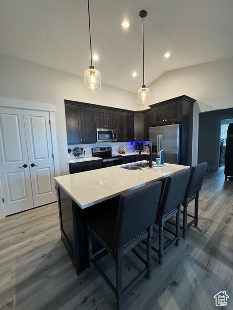 Kitchen with appliances with stainless steel finishes, light wood-style floors, vaulted ceiling, a breakfast bar area, and light stone countertops