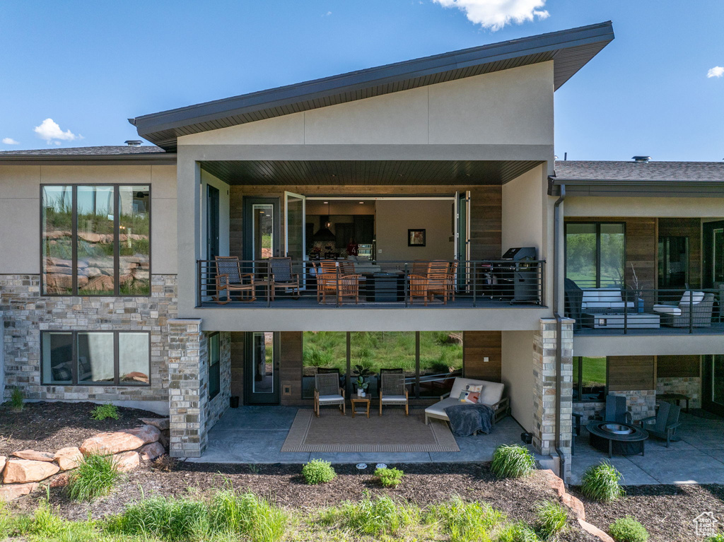 Rear view of house with stone siding, a patio area, a balcony, and stucco siding