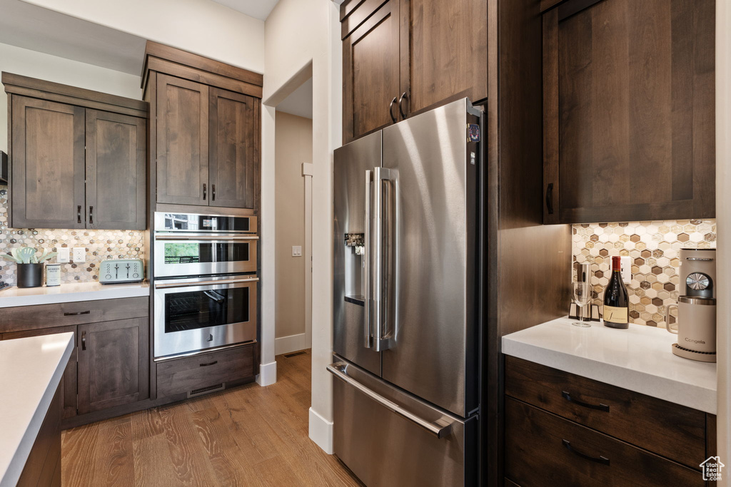 Kitchen featuring stainless steel appliances, backsplash, light countertops, light wood-style flooring, and dark brown cabinetry