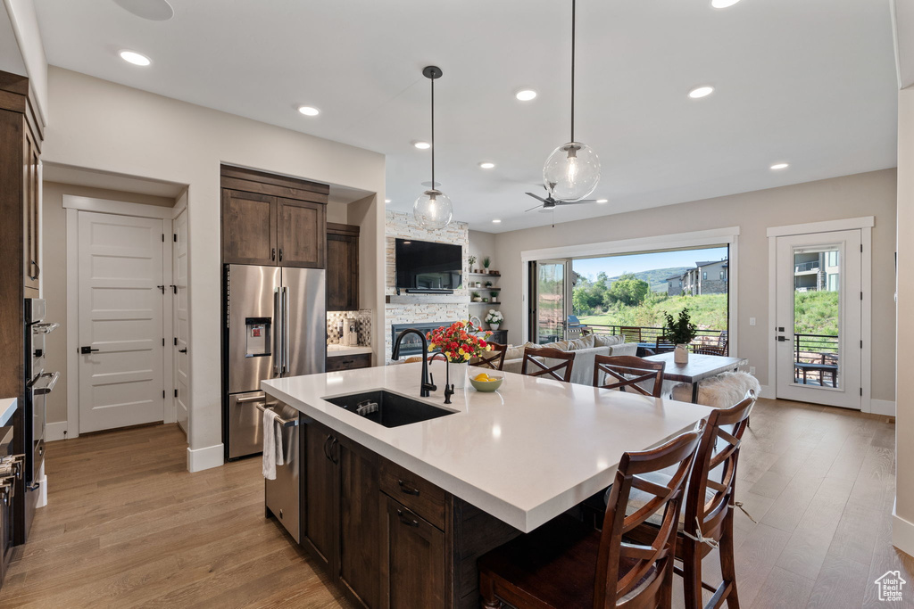 Kitchen with stainless steel appliances, dark brown cabinetry, a kitchen breakfast bar, light wood-type flooring, and light countertops