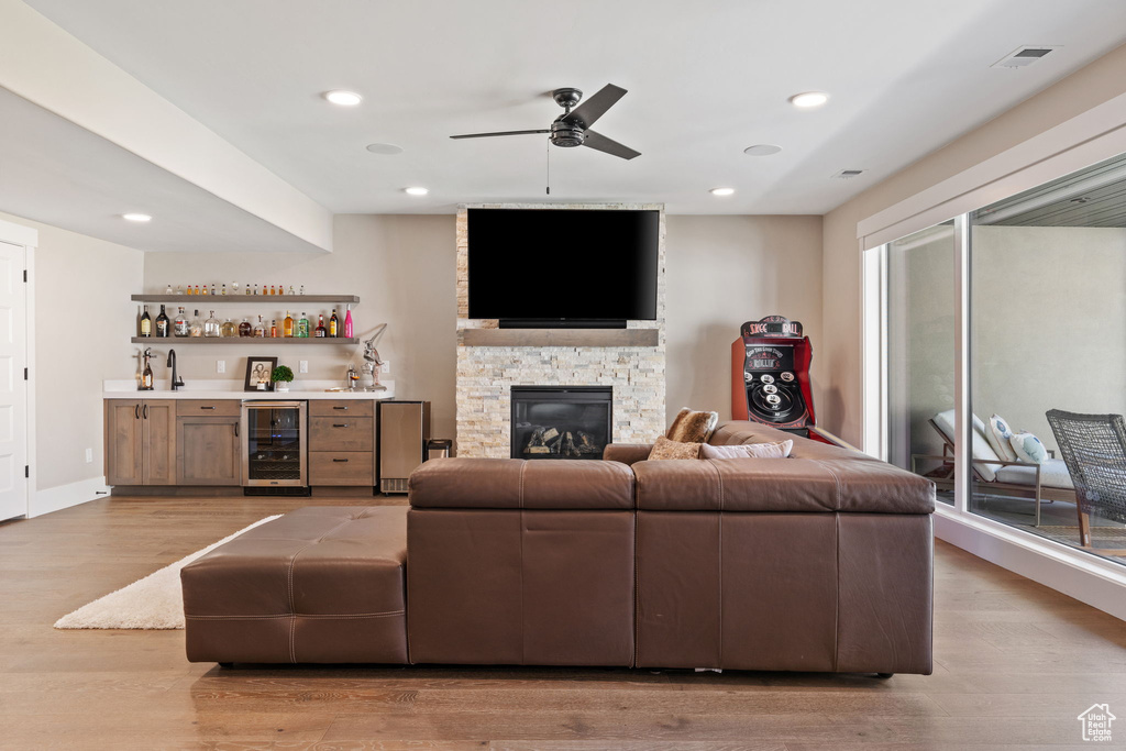 Living room featuring wine cooler, bar, ceiling fan, light wood-style floors, and a fireplace