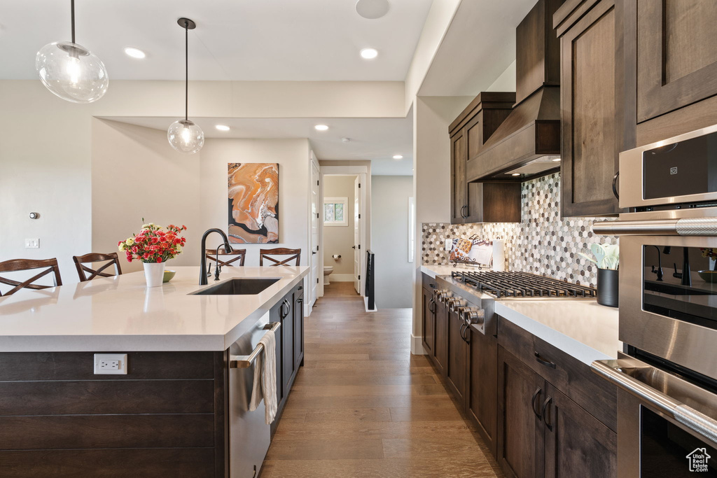 Kitchen with appliances with stainless steel finishes, light countertops, light wood-type flooring, dark brown cabinetry, and tasteful backsplash