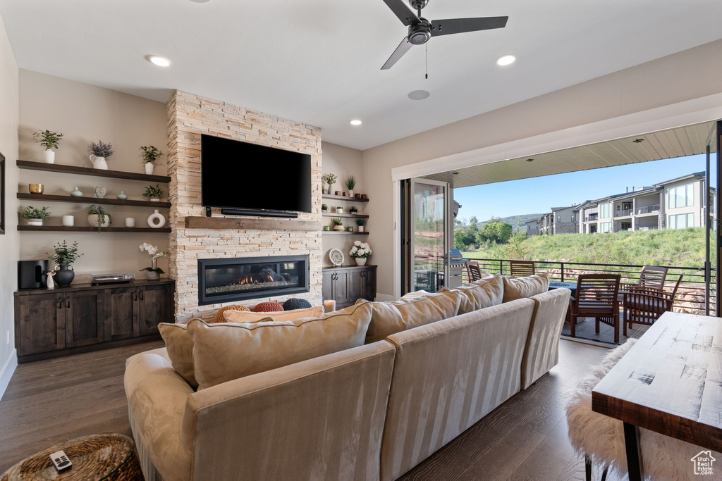 Living area with ceiling fan, dark wood-type flooring, a stone fireplace, and recessed lighting