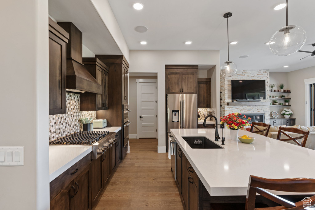 Kitchen with dark brown cabinetry, light countertops, stainless steel appliances, backsplash, and hanging light fixtures