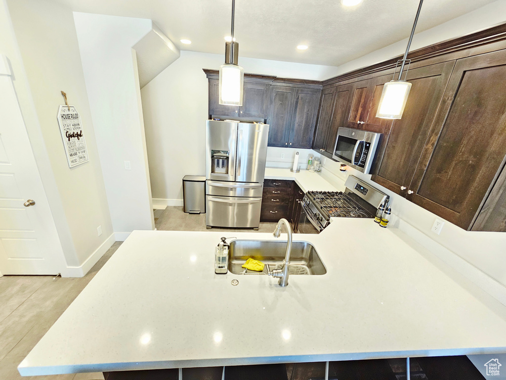 Kitchen featuring appliances with stainless steel finishes, dark brown cabinets, hanging light fixtures, a peninsula, and recessed lighting