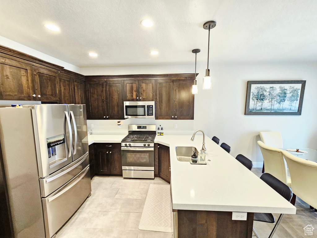 Kitchen featuring appliances with stainless steel finishes, a peninsula, dark brown cabinetry, recessed lighting, and light countertops