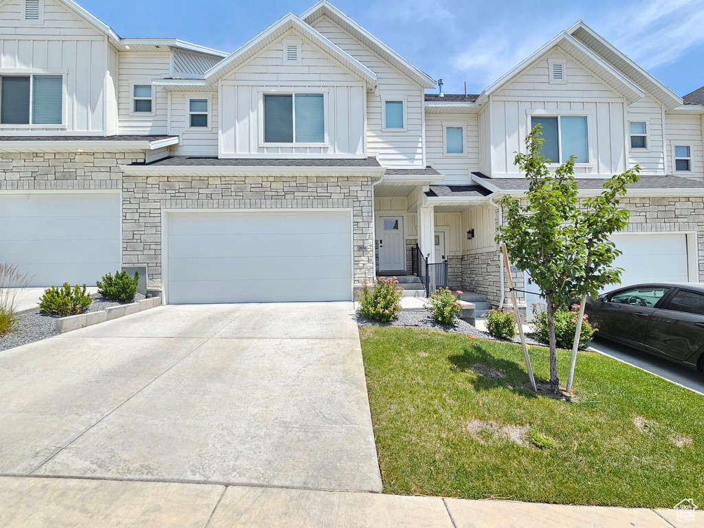 Townhome / multi-family property with board and batten siding, driveway, an attached garage, and stone siding