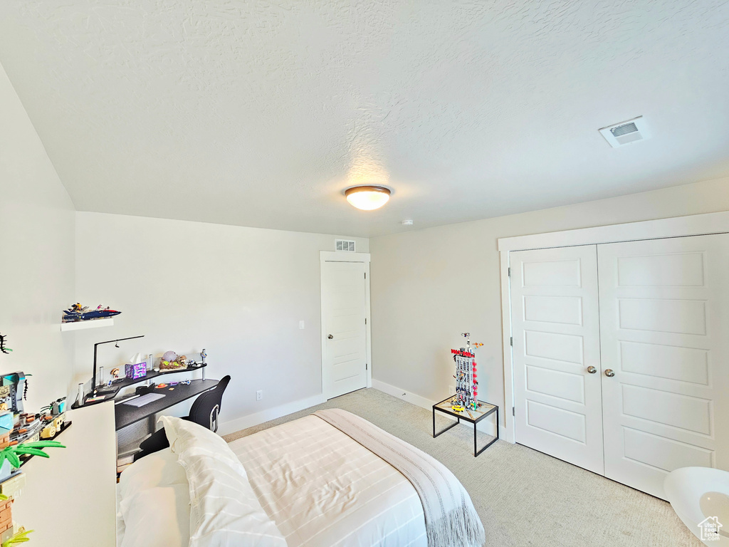 Bedroom featuring light carpet, a textured ceiling, and a closet