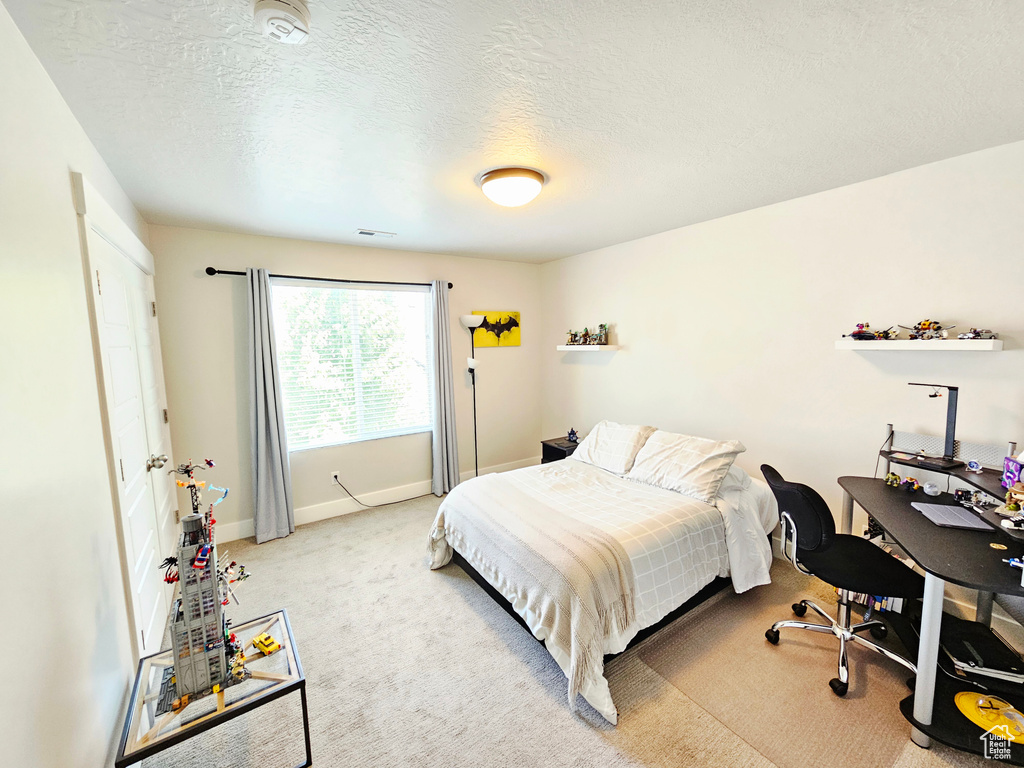 Bedroom with light colored carpet, an office area, and a textured ceiling