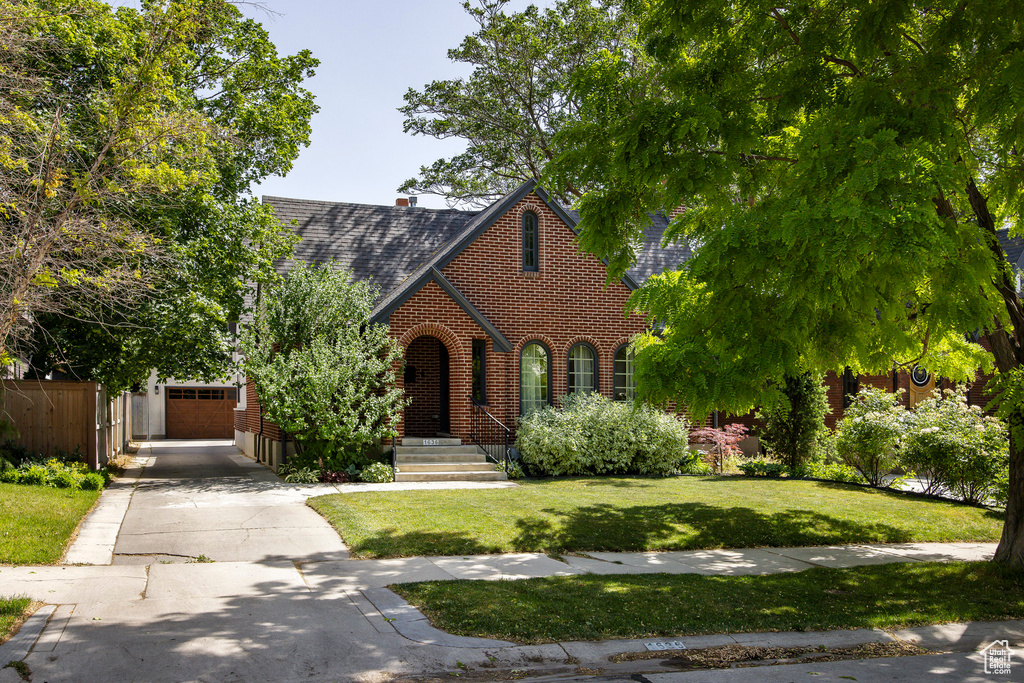 Tudor home with driveway, a shingled roof, and brick siding