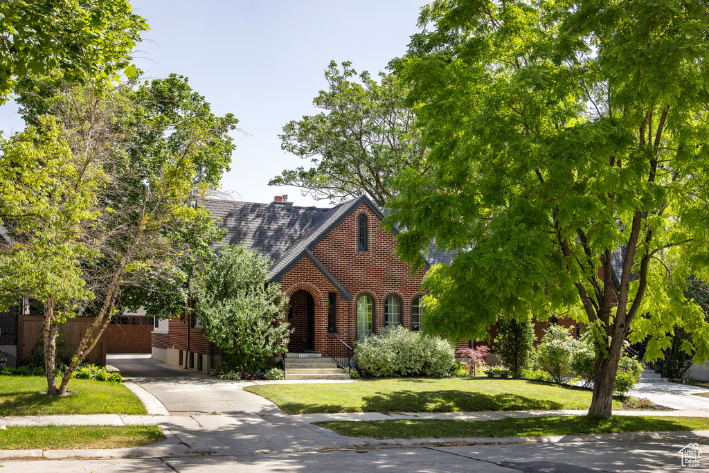 English style home with brick siding, driveway, a front yard, and a shingled roof