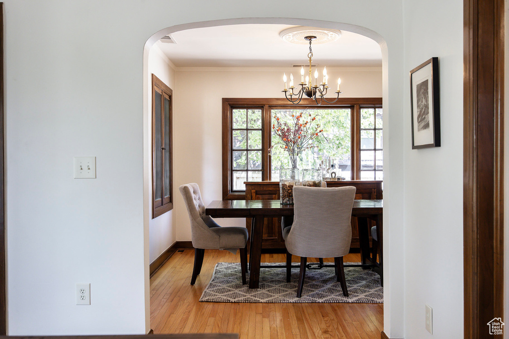 Dining room with arched walkways, wood finished floors, a chandelier, and crown molding