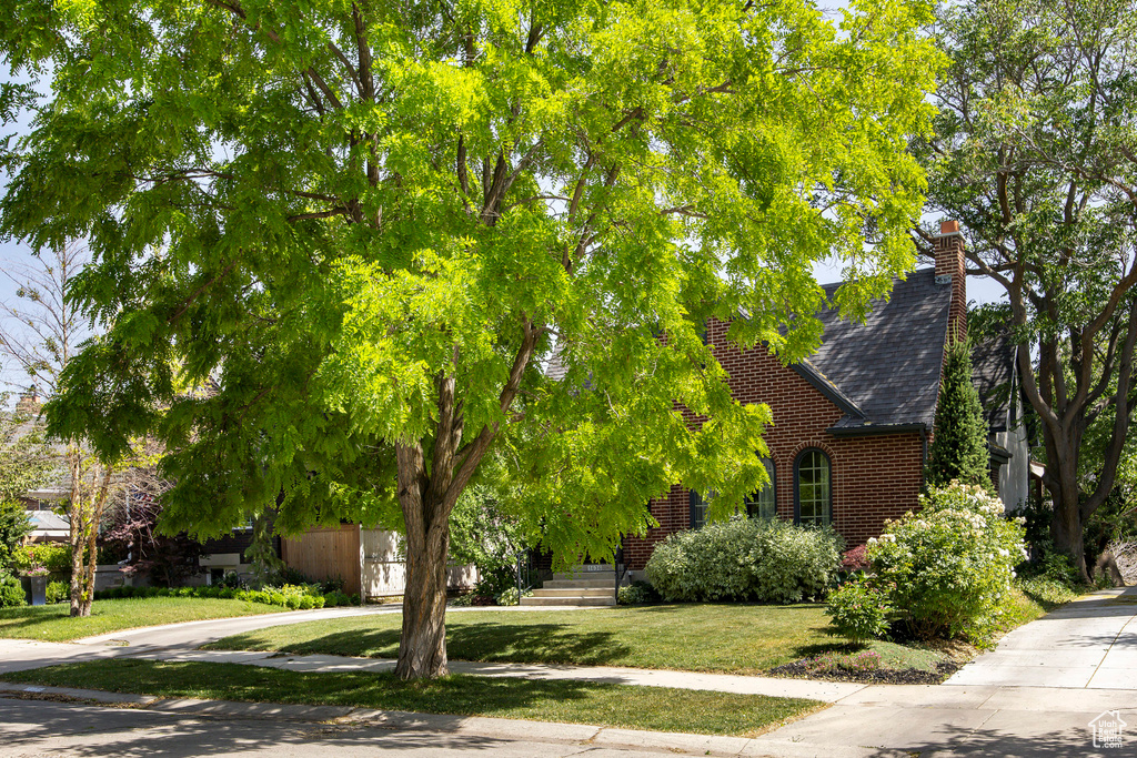 View of front facade with brick siding, a chimney, a front lawn, and roof with shingles