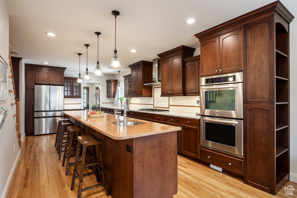 Kitchen featuring stainless steel appliances, open shelves, wall chimney range hood, backsplash, and light wood-type flooring