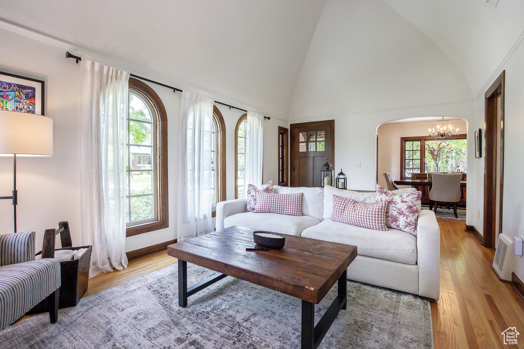 Living area with a chandelier, healthy amount of natural light, light wood-type flooring, and vaulted ceiling