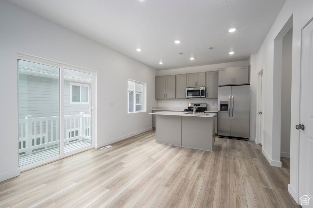 Kitchen featuring appliances with stainless steel finishes, gray cabinetry, recessed lighting, an island with sink, and light wood-style floors