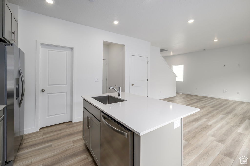 Kitchen with stainless steel appliances, light wood-style floors, open floor plan, a center island with sink, and recessed lighting