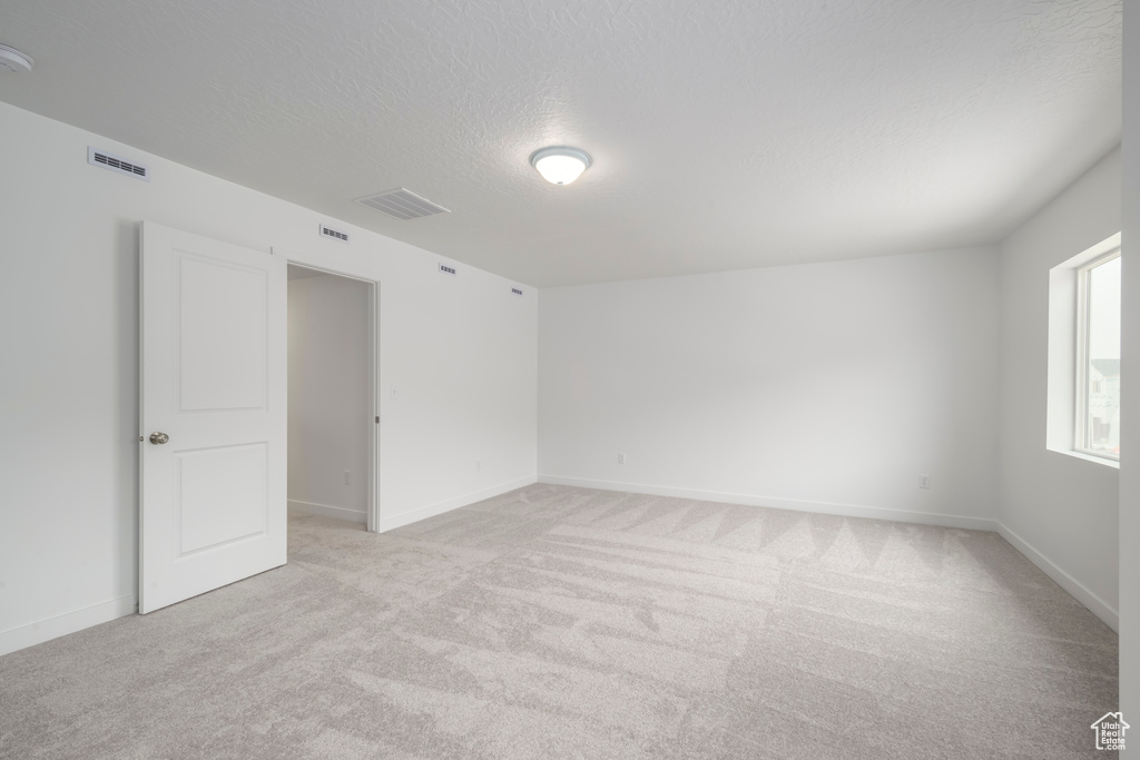 Unfurnished room featuring light carpet, a textured ceiling, and a smoke detector