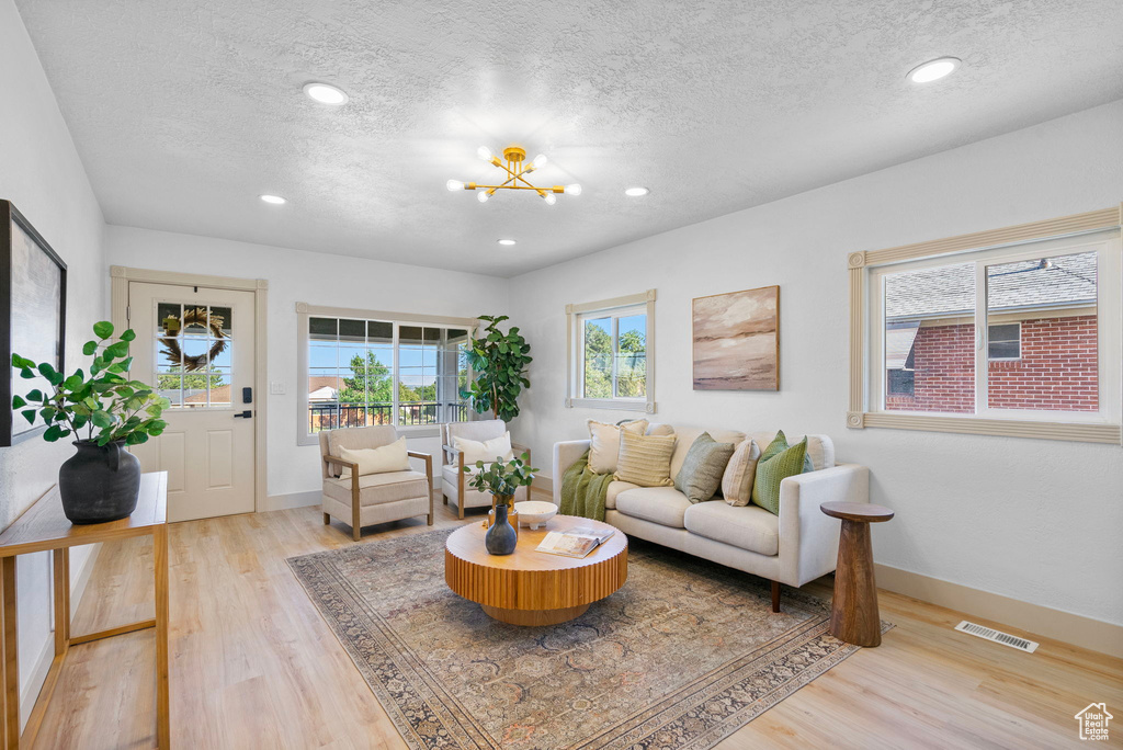 Living area with a textured ceiling, light wood-type flooring, a chandelier, and recessed lighting