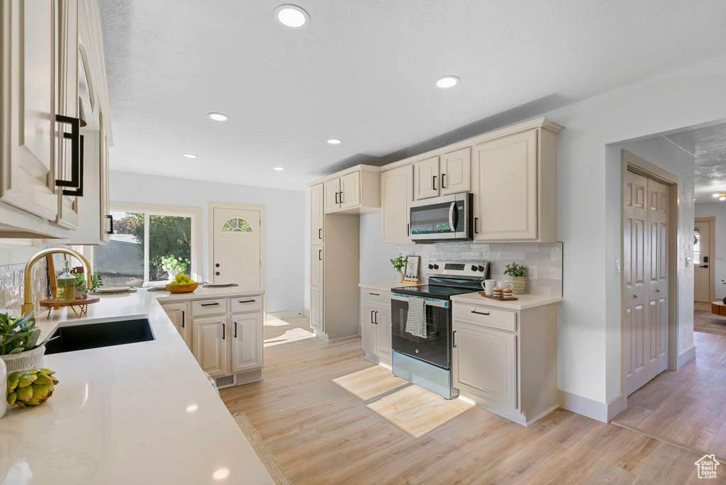 Kitchen featuring stainless steel appliances, light wood finished floors, light countertops, backsplash, and recessed lighting