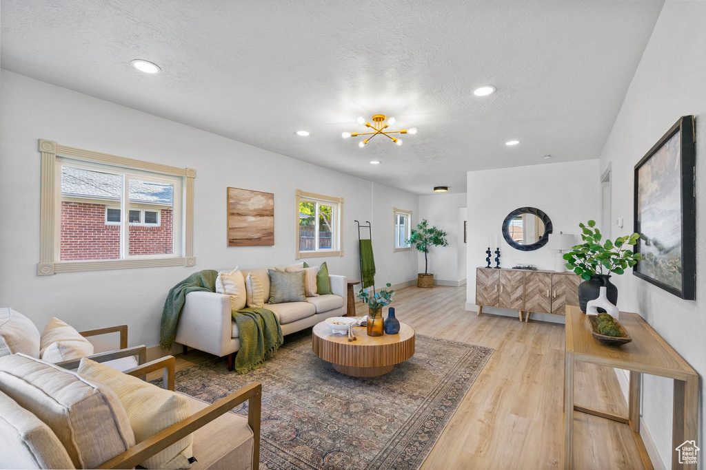 Living room featuring light wood-type flooring, a chandelier, recessed lighting, and a textured ceiling