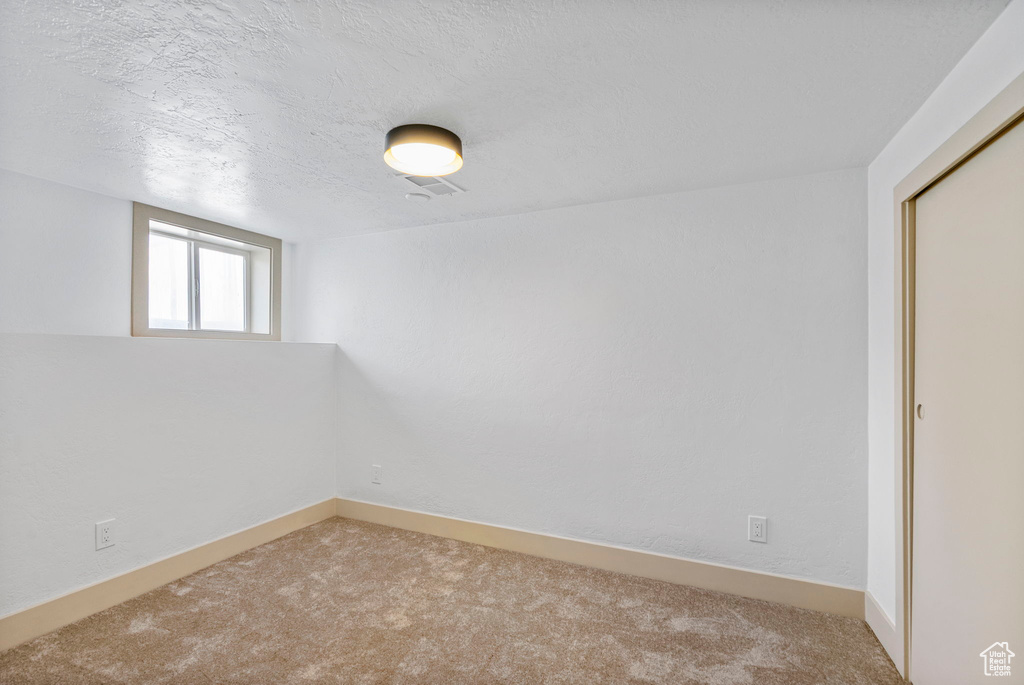 Empty room with light colored carpet and a textured ceiling