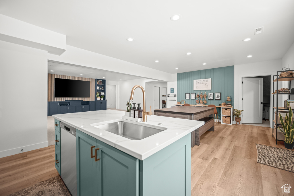 Kitchen with dishwasher, a kitchen island with sink, recessed lighting, light stone counters, and light wood-style flooring