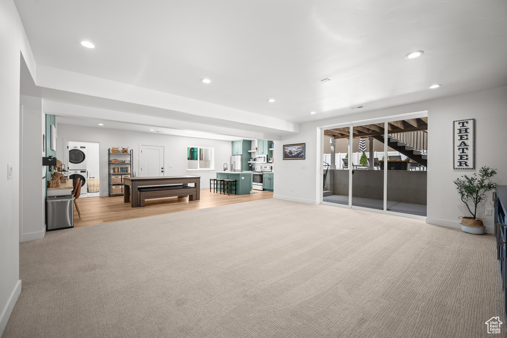 Living area with stacked washing machine and dryer, recessed lighting, light colored carpet, and stairway