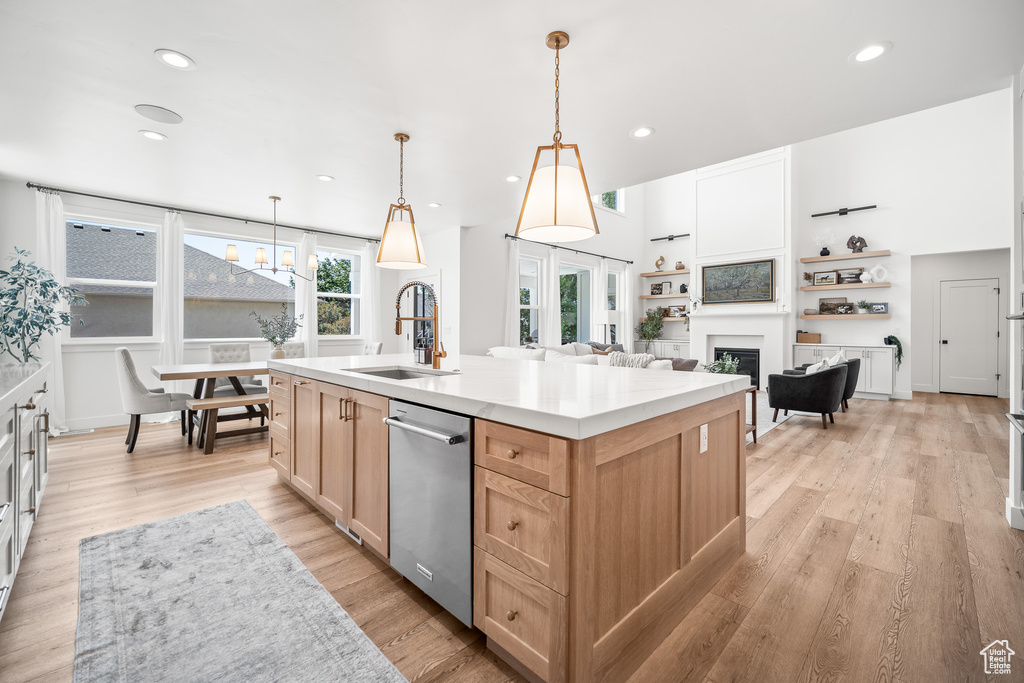 Kitchen featuring stainless steel dishwasher, light brown cabinets, a glass covered fireplace, a kitchen island with sink, and light wood-type flooring