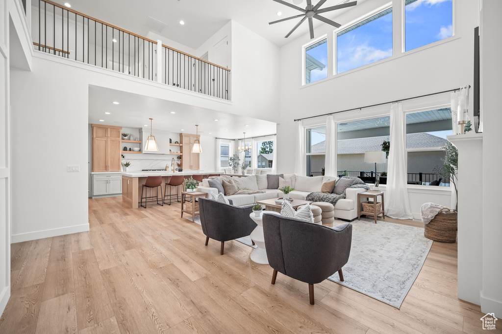 Living room with a towering ceiling, light wood-style flooring, healthy amount of natural light, a ceiling fan, and recessed lighting