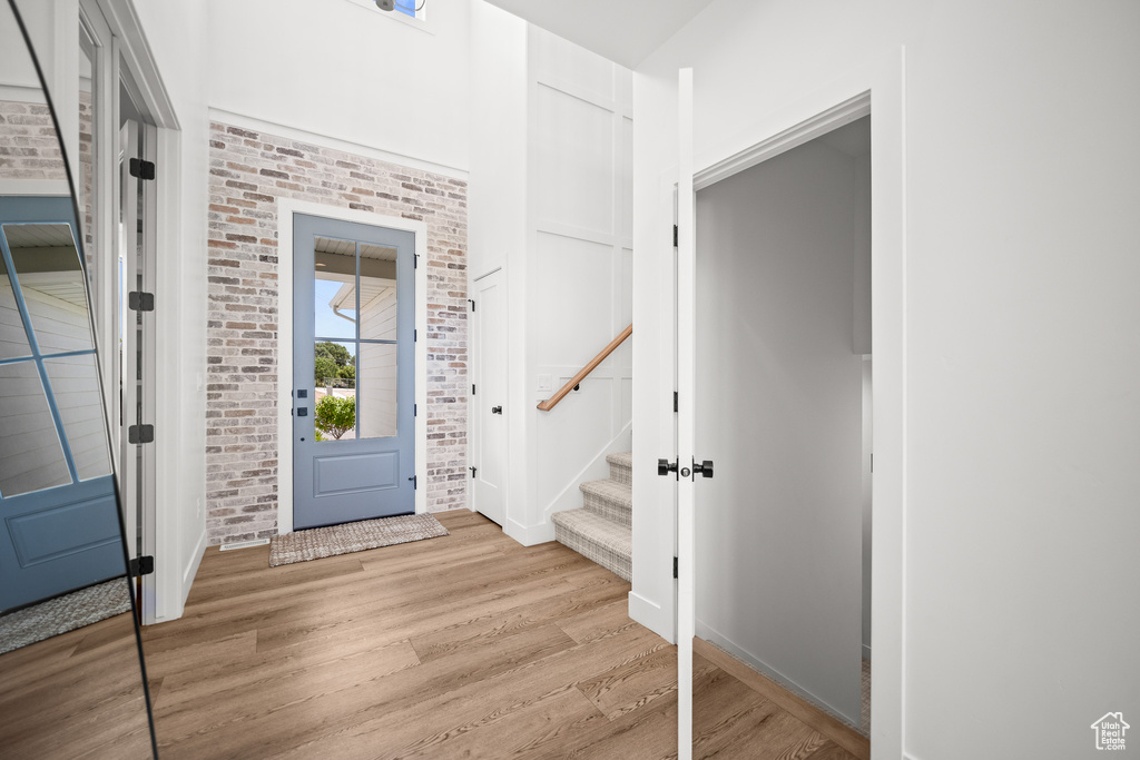 Foyer entrance with light wood-style flooring, brick wall, and stairway