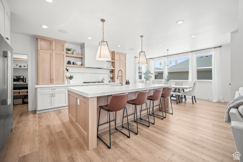 Kitchen featuring light countertops, light brown cabinetry, open shelves, recessed lighting, and an island with sink