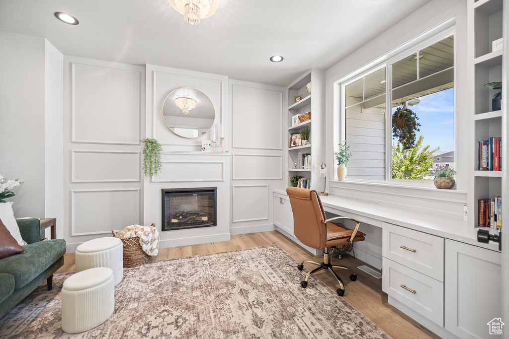 Office space featuring built in desk, light wood-style floors, a glass covered fireplace, recessed lighting, and built in features