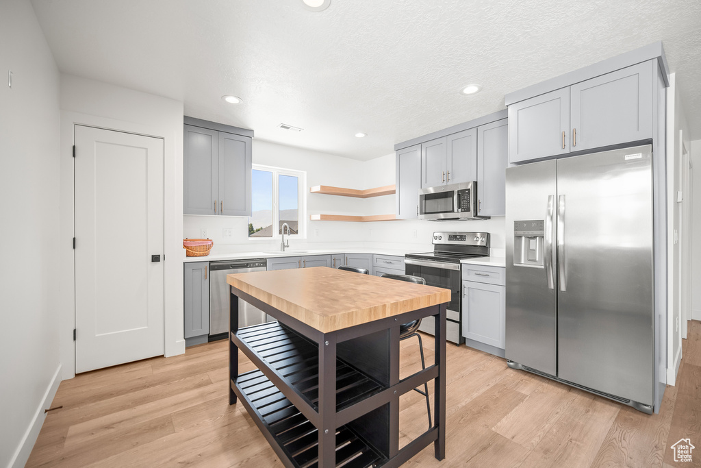 Kitchen featuring appliances with stainless steel finishes, gray cabinets, open shelves, light wood-type flooring, and recessed lighting