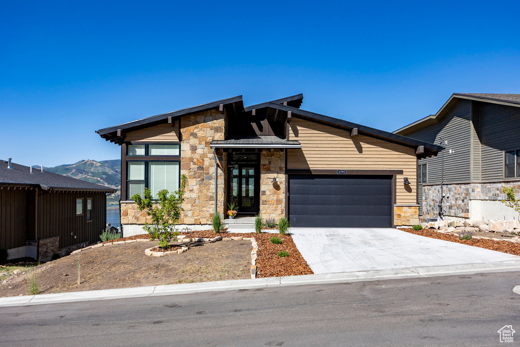View of front of home featuring stone siding, a garage, concrete driveway, and a mountain view
