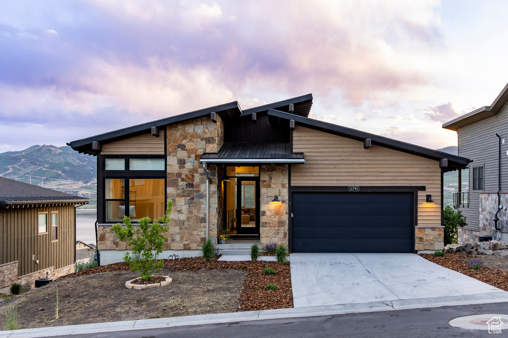 Contemporary house featuring stone siding, an attached garage, driveway, and a mountain view