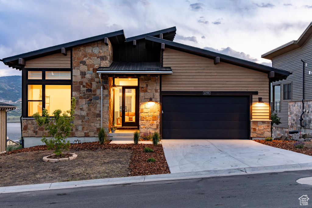 Modern home featuring stone siding, an attached garage, and driveway