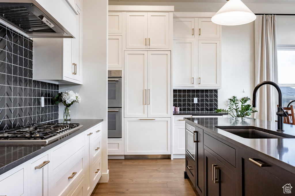 Kitchen with appliances with stainless steel finishes, exhaust hood, dark countertops, and white cabinetry