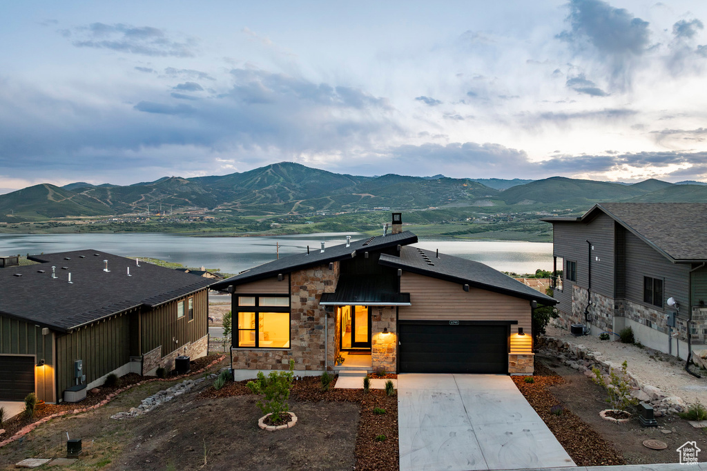View of front facade featuring stone siding, a water and mountain view, driveway, and a garage