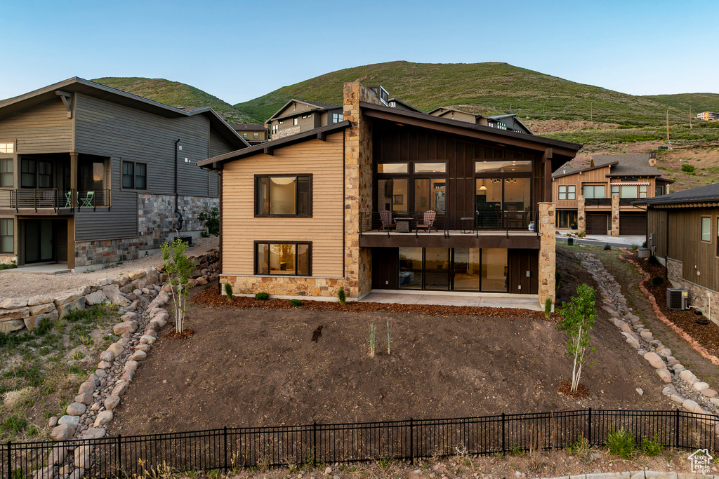 Back of house with a mountain view, stone siding, a balcony, and a patio