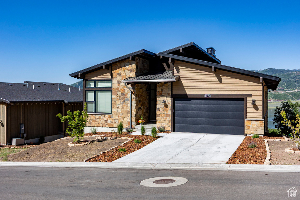 View of front of property featuring stone siding, a garage, concrete driveway, a standing seam roof, and a metal roof