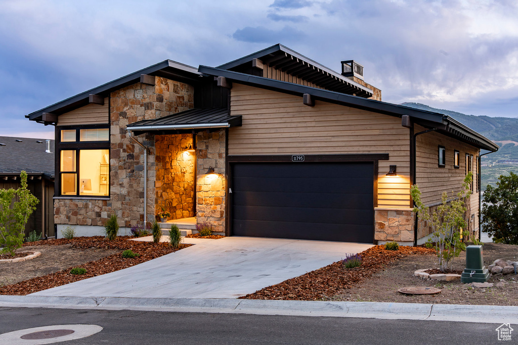 Modern home featuring stone siding, a standing seam roof, driveway, a garage, and a metal roof